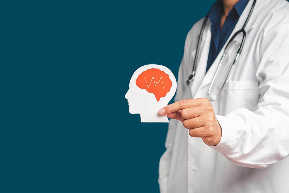 Midsection of doctor in uniform holding a white head with a red brain symbol made from paper while standing on a blue background