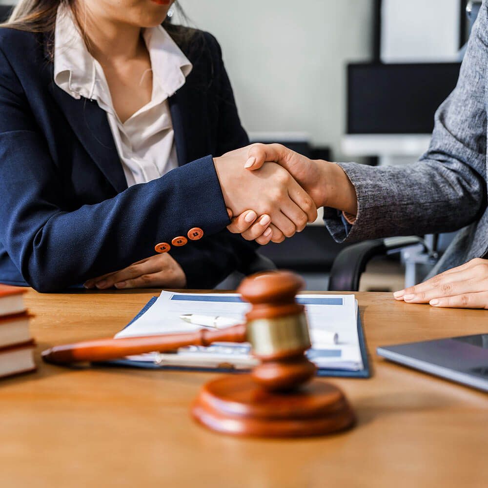 Two female lawyers in business suits shake hands at wooden desk, finalizing legal agreement