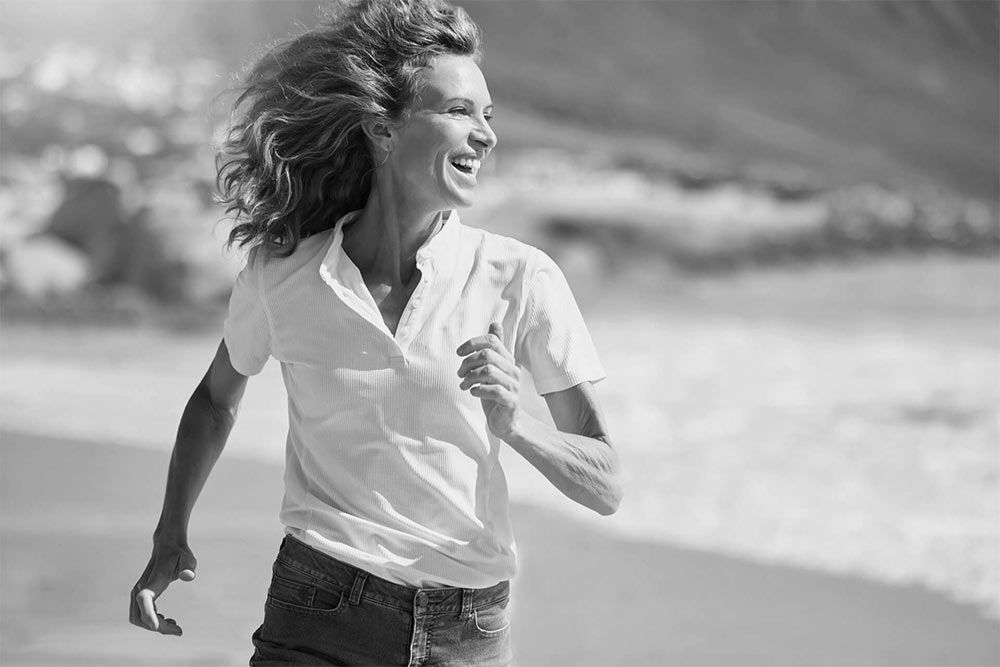 Cheerful mature woman running on the beach on a sunny day
