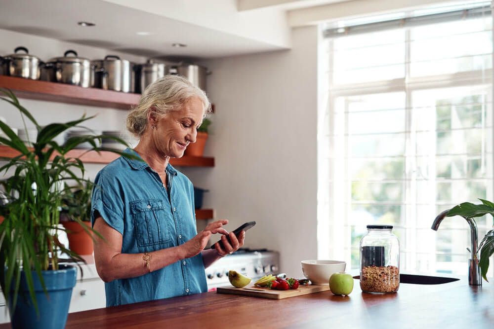 Mature woman, kitchen and cellphone for recipe, cooking and read for instructions online