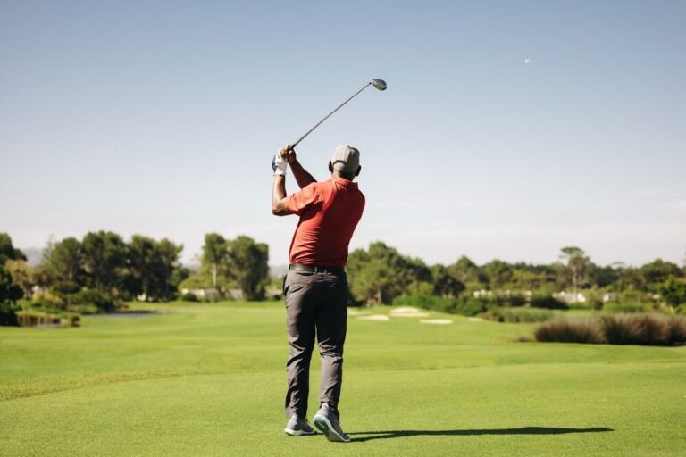 Man swinging golf club in perfect follow through position during an approach shot on a sunny day
