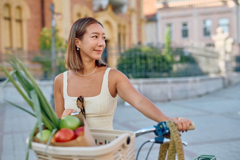 Young woman joyfully riding a bicycle through the city, happily carrying fresh groceries in the front basket while embracing an active lifestyle