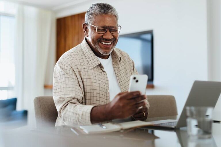 Happy mature male using his phone while sitting at a desk, connecting and staying in touch