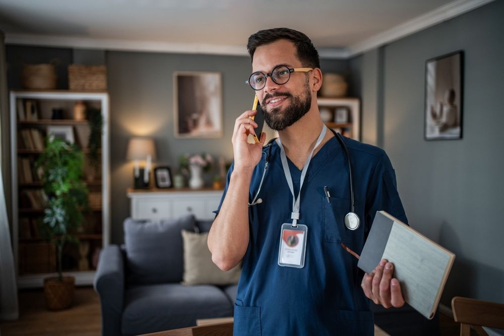 Young man doctor wearing dark blue scrubs and glasses smiling while talking on a smartphone
