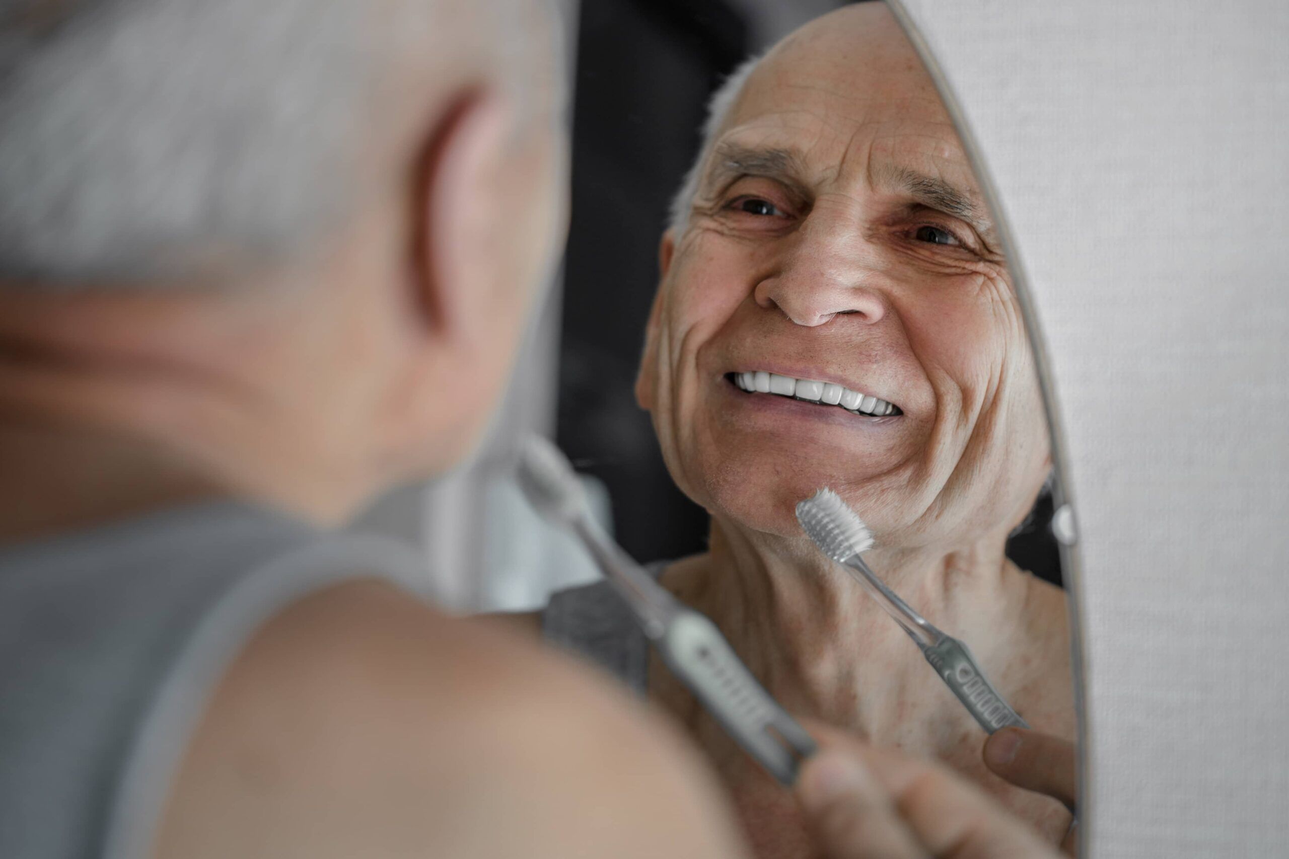 Smiling old man brushing his teeth prosthesis with toothbrush.