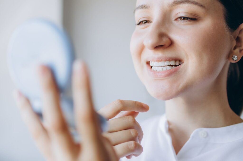 Young woman is checking her teeth for imperfections in a small mirror