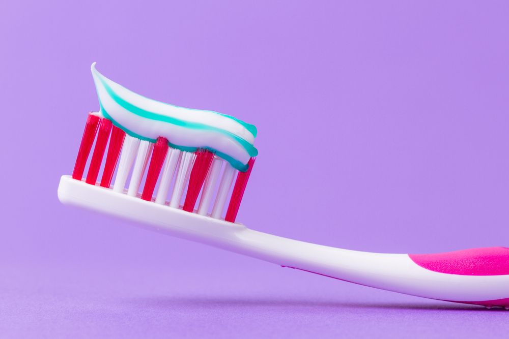 A pink toothbrush with toothpaste on a purple background