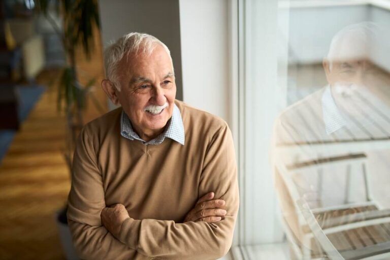Happy mature man looking through window at home