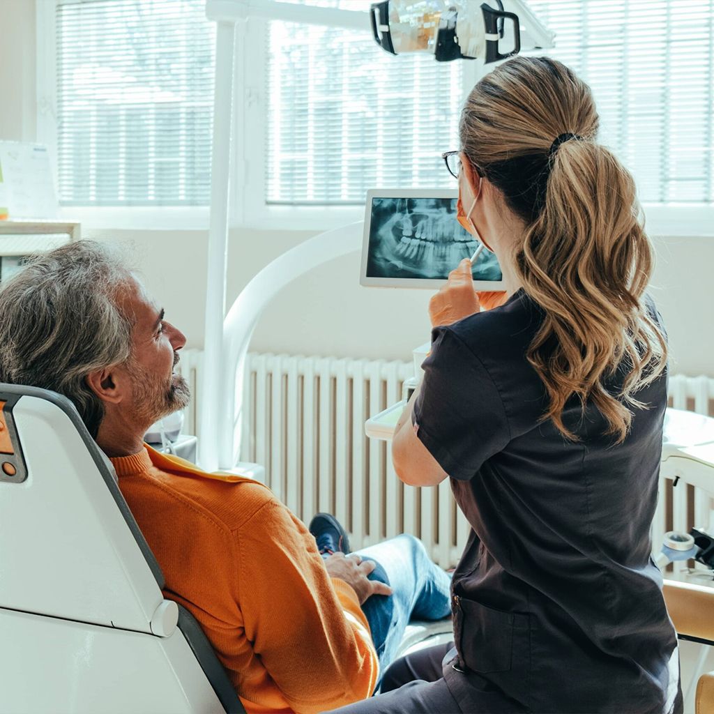An Anonymous Female Dentist Explaining Teeth X-ray on a Digital Tablet to Smiling Mature Patient at Dentist's Office