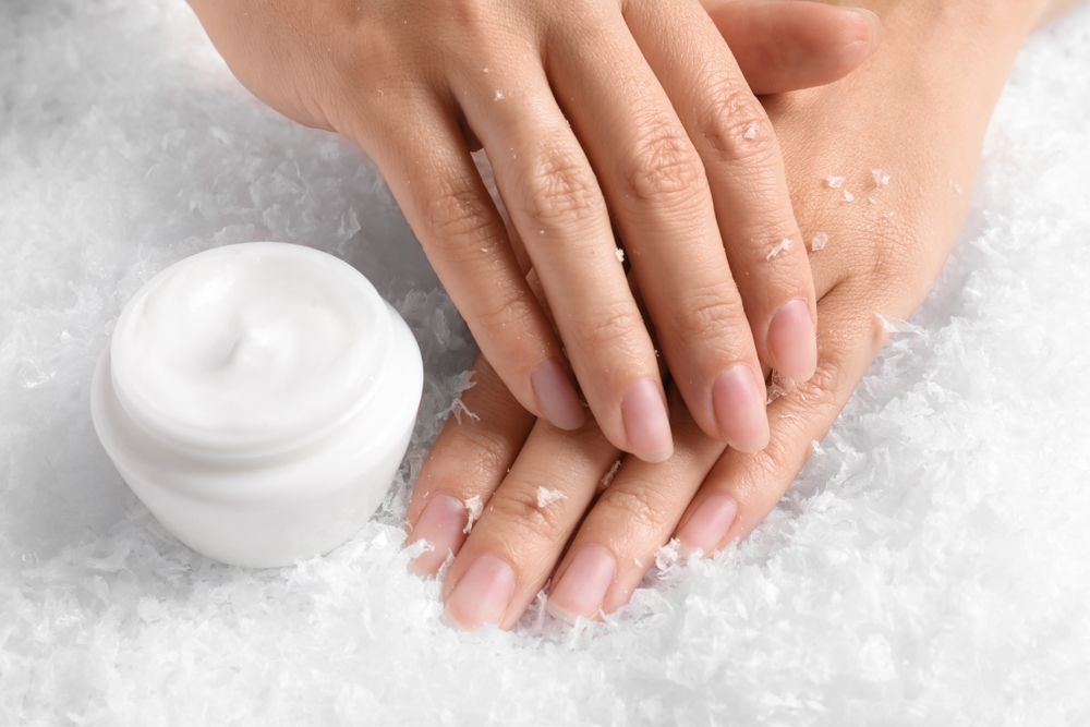 Woman holding hands near jar of cream on decorative snow.