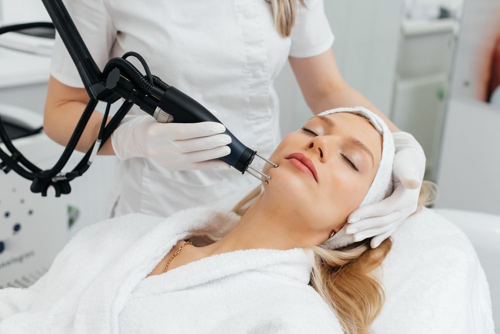 A young girl gets a charcoal peeling for the skin of the face in a beauty salon. Laser pulses cleanse the skin.