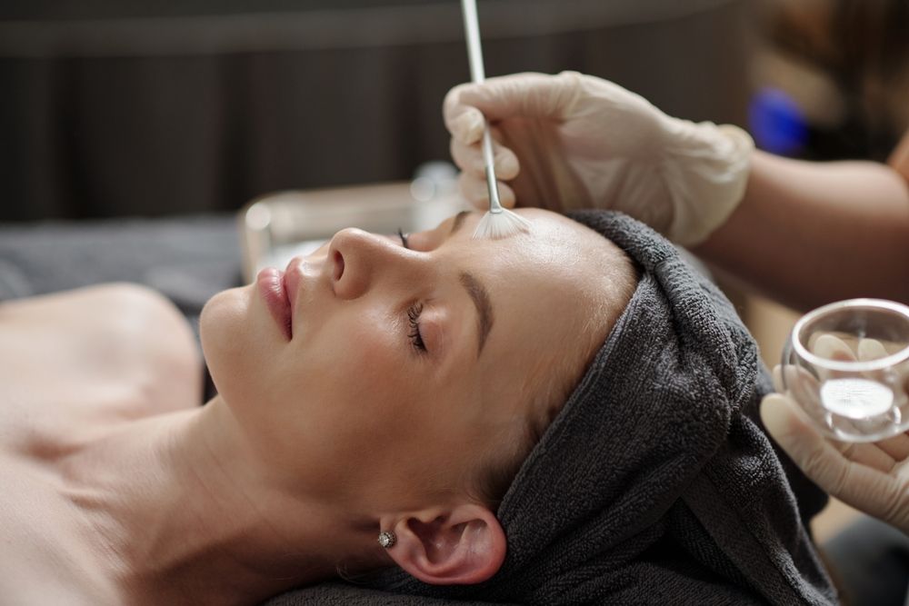 Esthetician applying glycolic acid peel on face of young woman