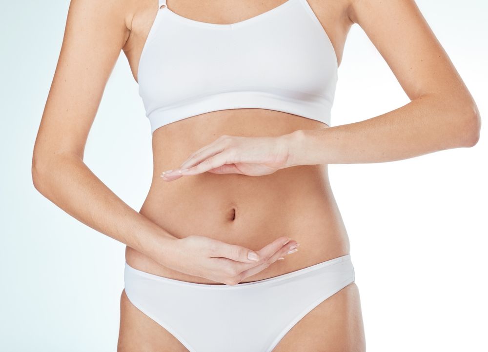 Woman, abdomen and hands for gut in studio, wellness and lingerie for self care on white background.