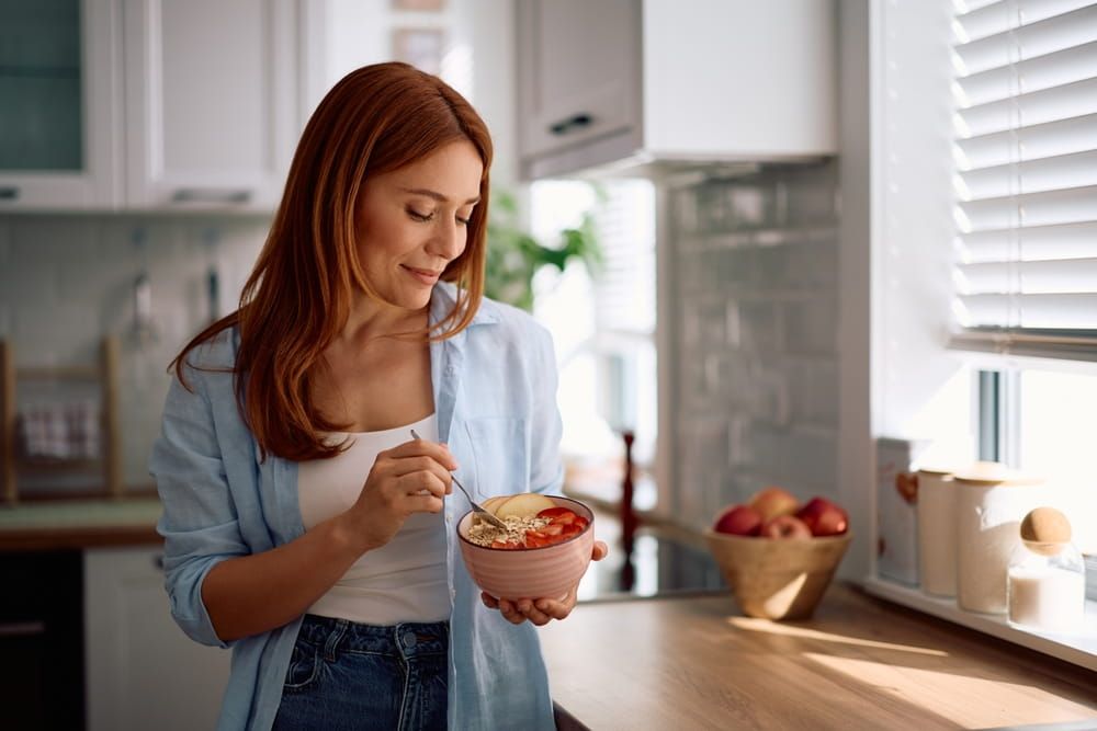 Smiling woman eating oatmeal with fresh fruit in the morning