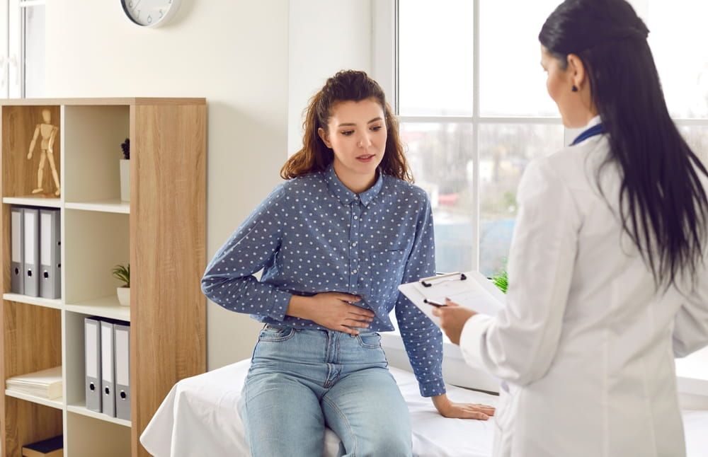 Female medical specialist consults young female patient who complains of abdominal pain discomfort due to menstrual pain, pancreatitis, gastritis or diarrhea.