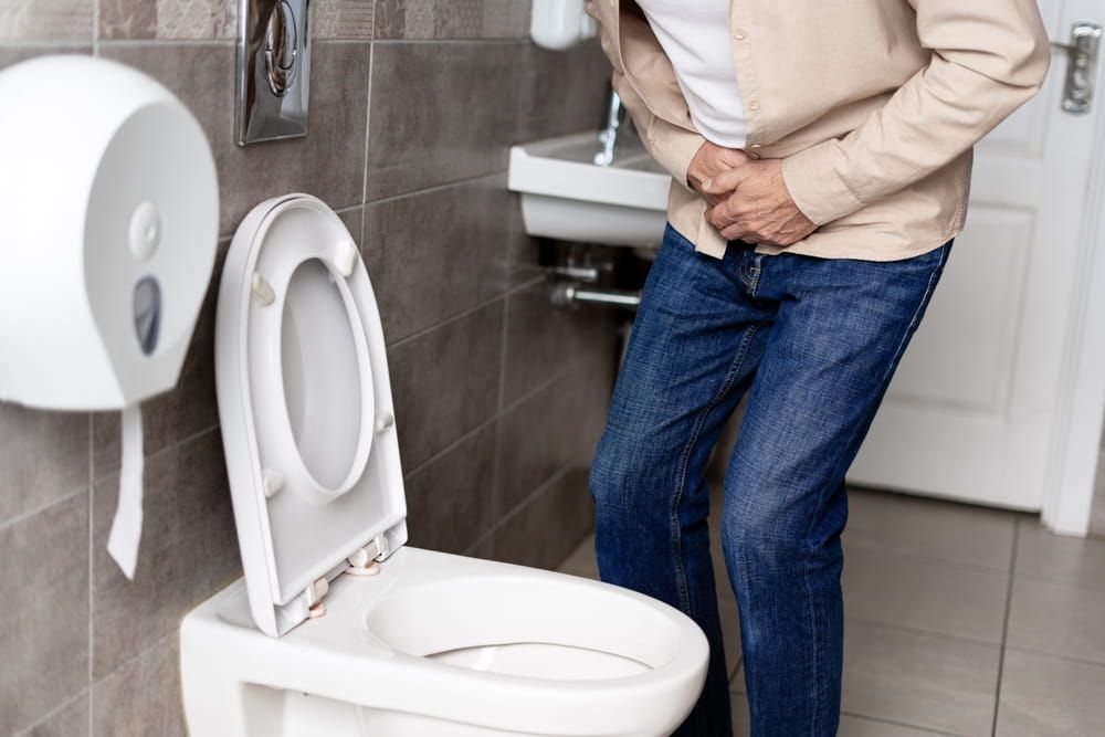 Elderly man experiencing discomfort from stomach or bladder pain while using a public toilet