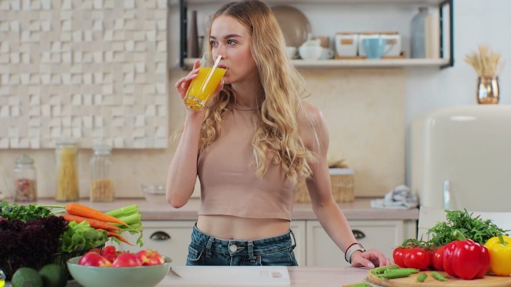 Woman drinking an orange juice at kitchen. Attractive sporty girl drinking freshly juice. Lifestyle and healthy nutrition concept.