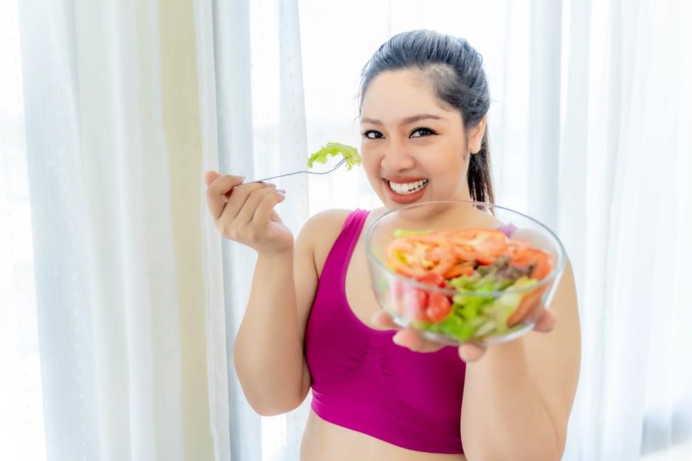 Cheerful plus-size woman enjoying a fresh vegetable salad,