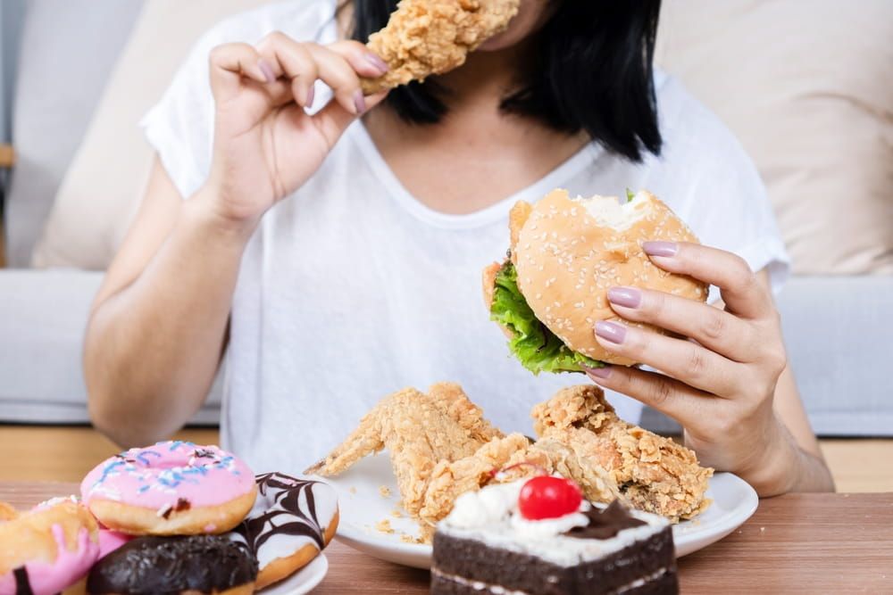woman eating fast food burger, fired chicken , donuts and desserts
