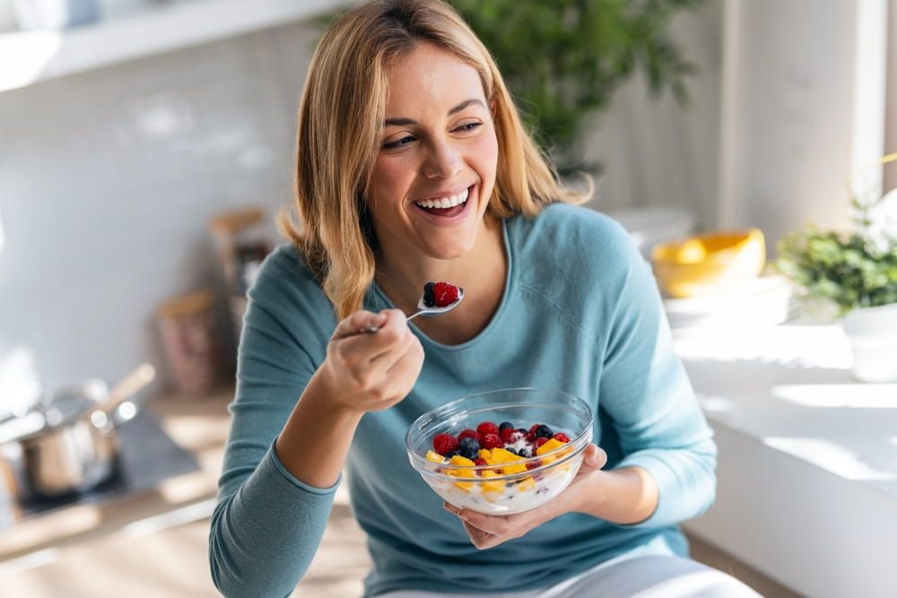 woman eating a healthy fruit bowl while sitting on the table in the kitchen at home