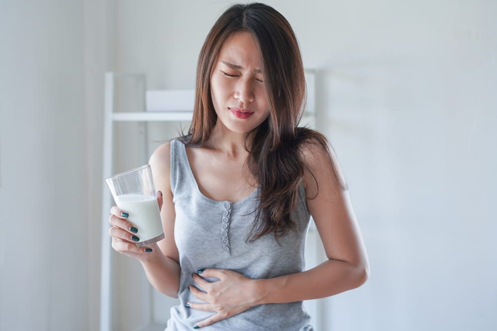 Asian woman with stomach ache and pain holding a glass of milk. Dairy intolerant, Lactose intolerance