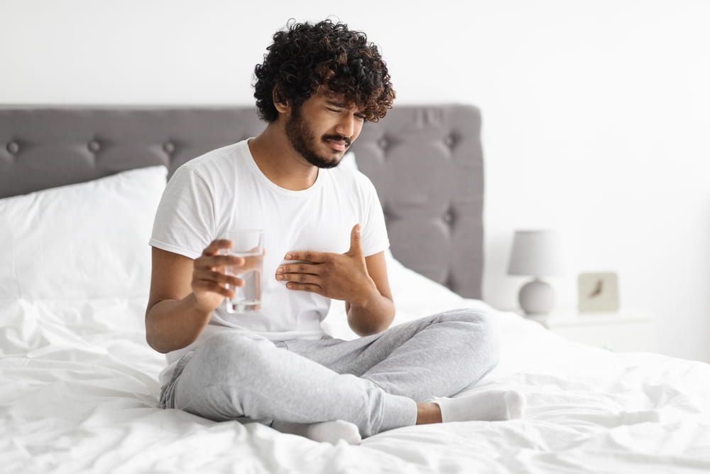Unhappy millennial indian guy suffering from heartburn, waking up in morning