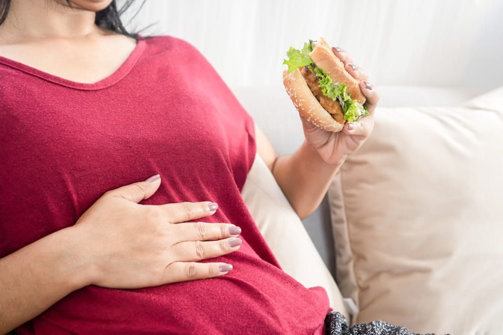 woman having stomachache or flatulence after eating burger, hand holding her abdominal