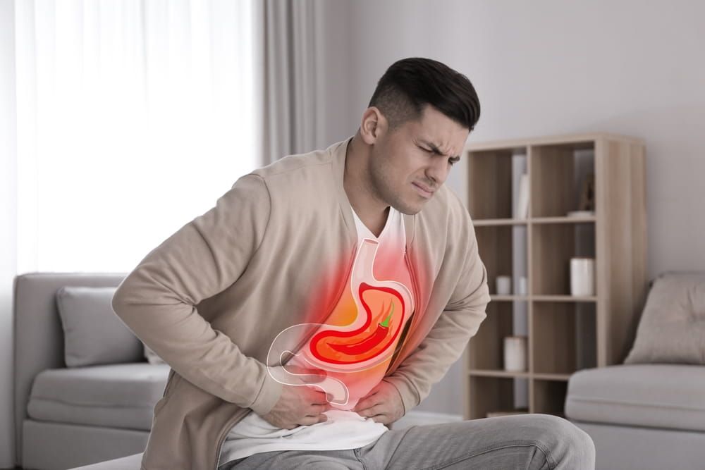 Man suffering from heartburn at home. Stomach with hot chili pepper symbolizing acid indigestion