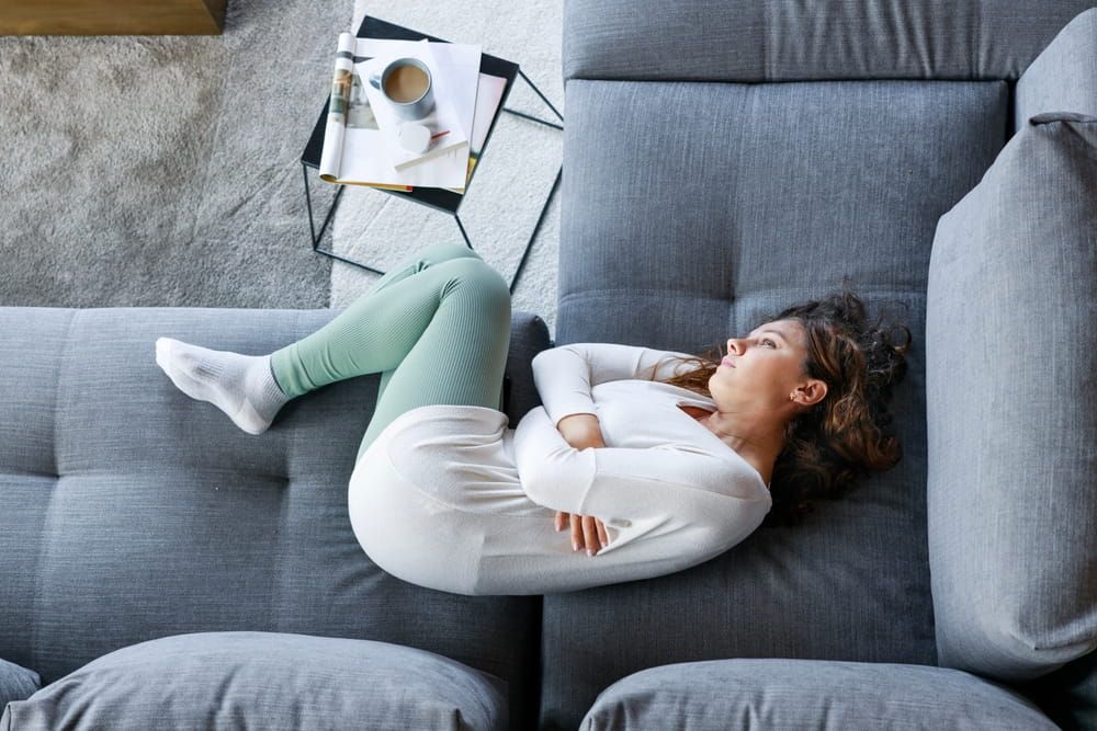 depressed young woman lying on couch, drowsing, feeling stress or suffering from abdominal pain