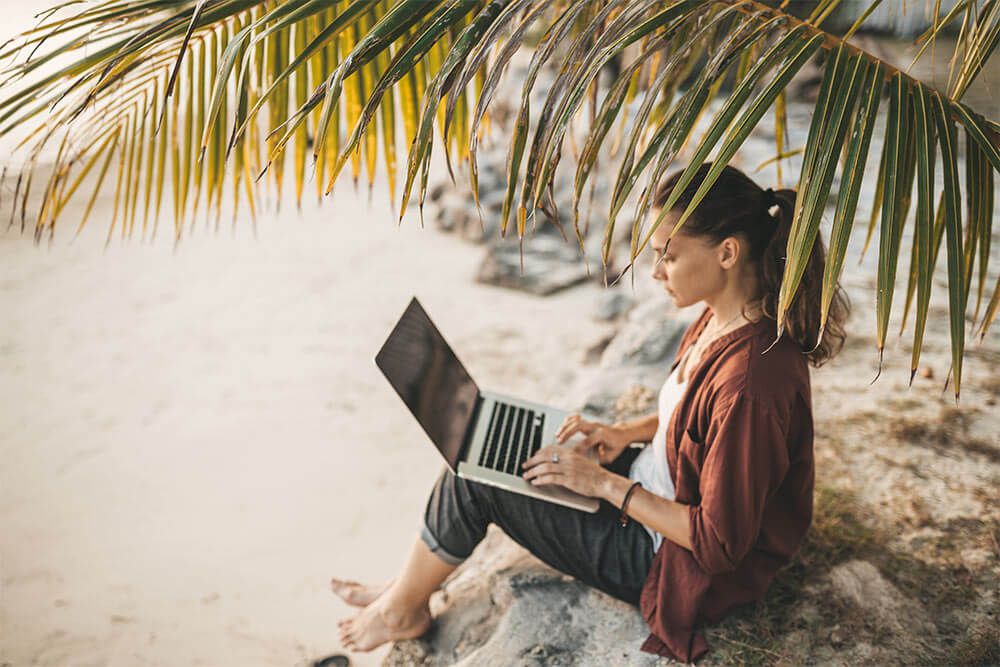 Woman sitting with laptop on the summer beach at sunset