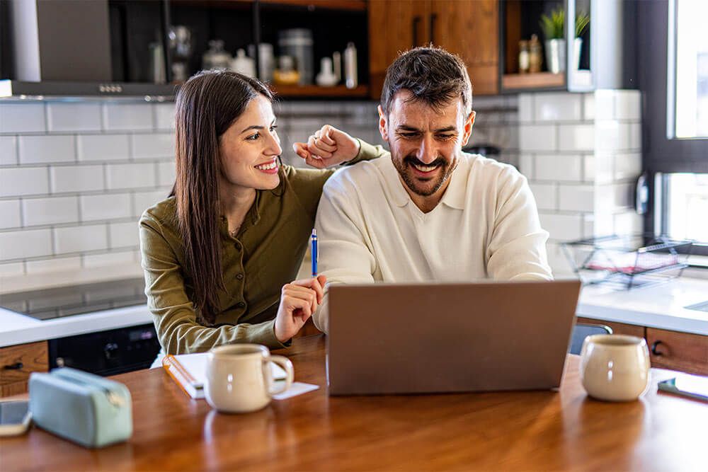 Happy couple smiling together while using a laptop