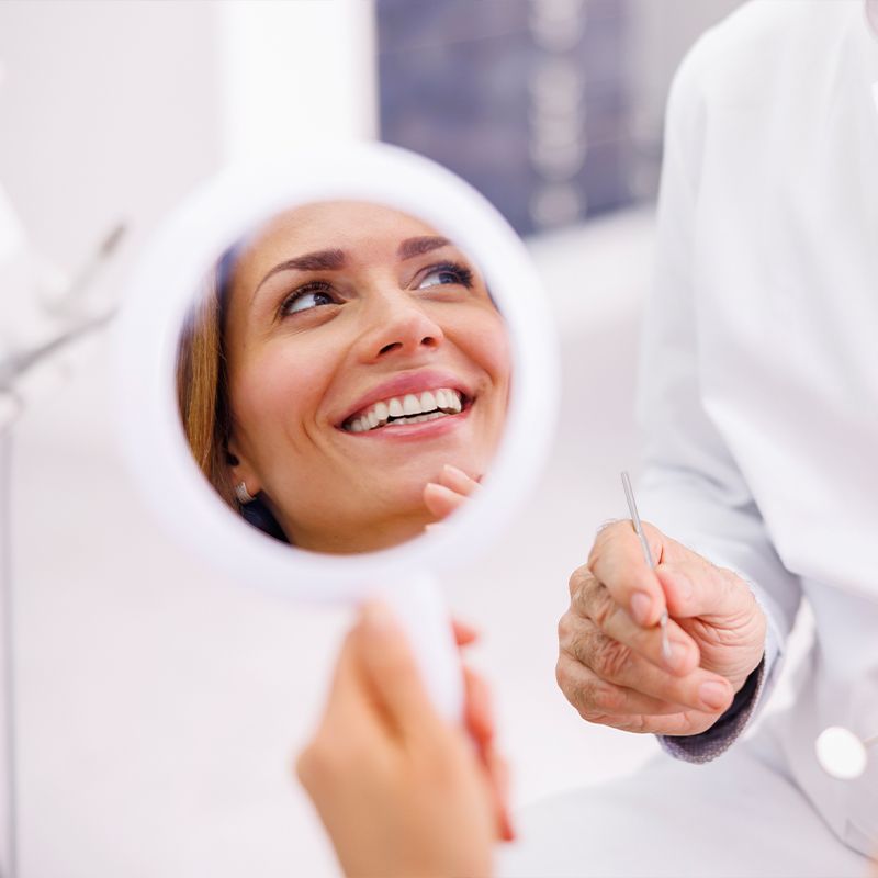 Woman looking in the mirror and smiling after checkup at dentist office