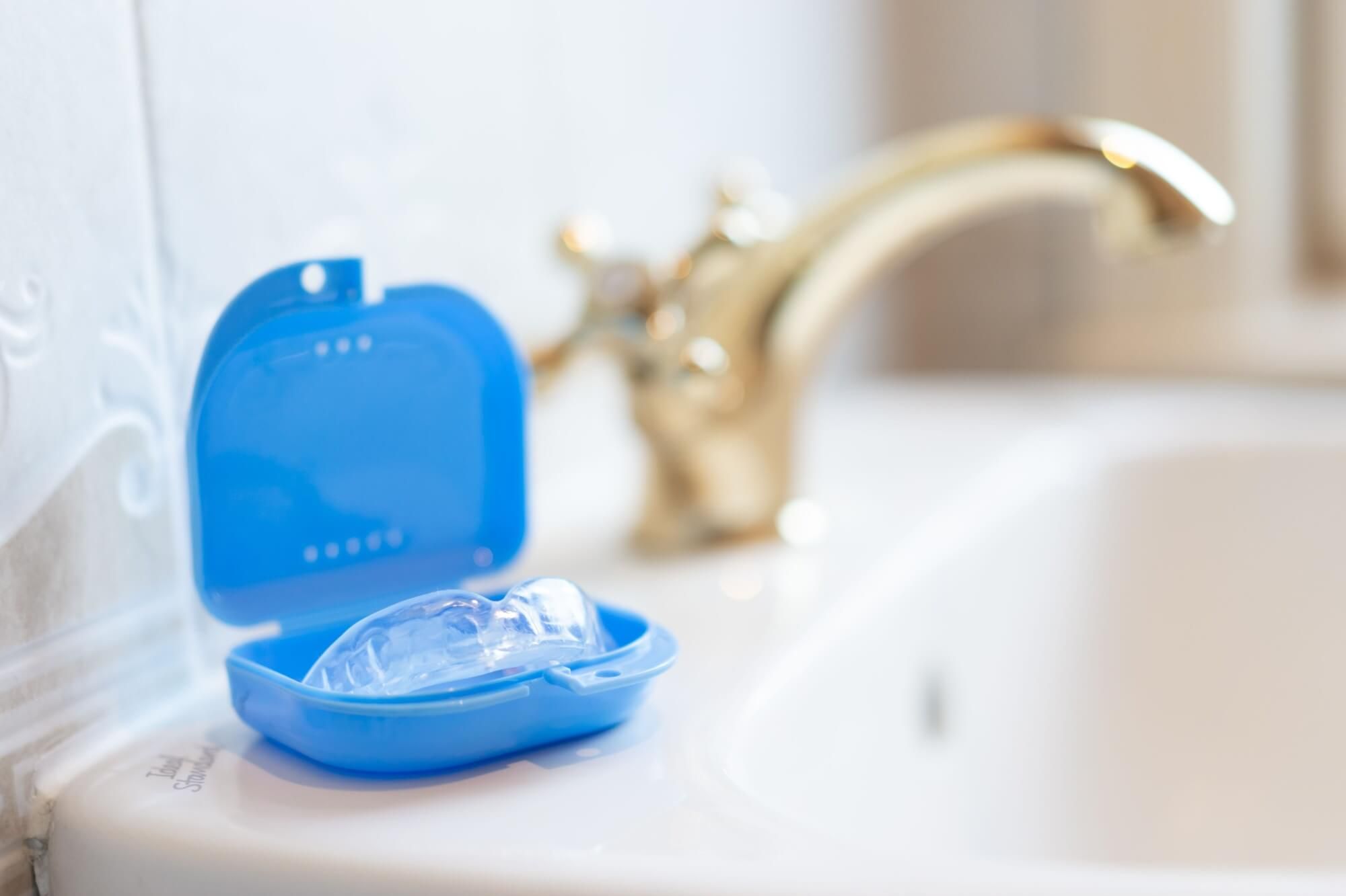 A night guard, used to protect teeth from grinding during sleep, is in its travel case on a sink