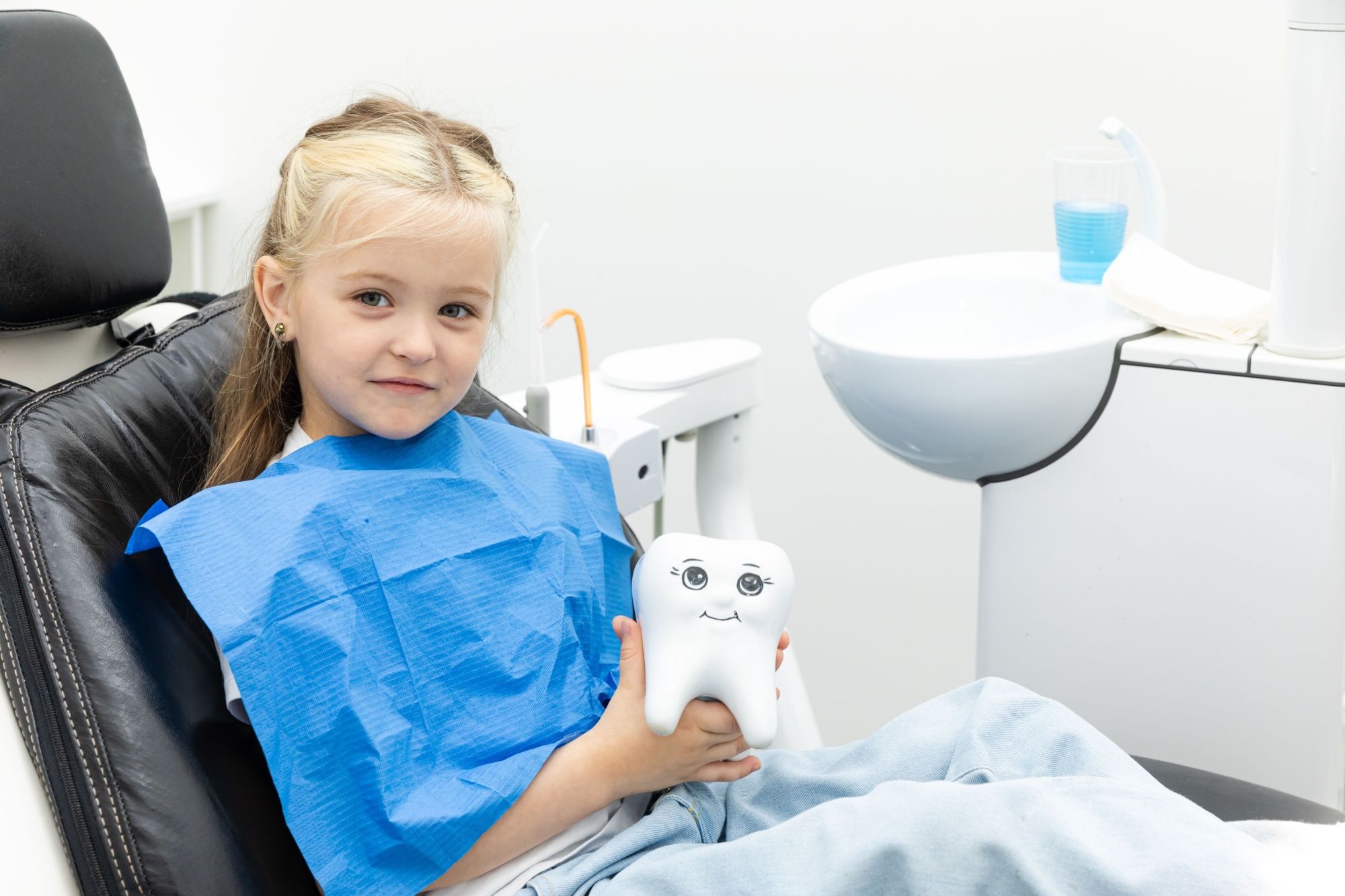 Happy little child sits in a dental chair and shows an artificial model of a child's tooth in a children's dental clinic