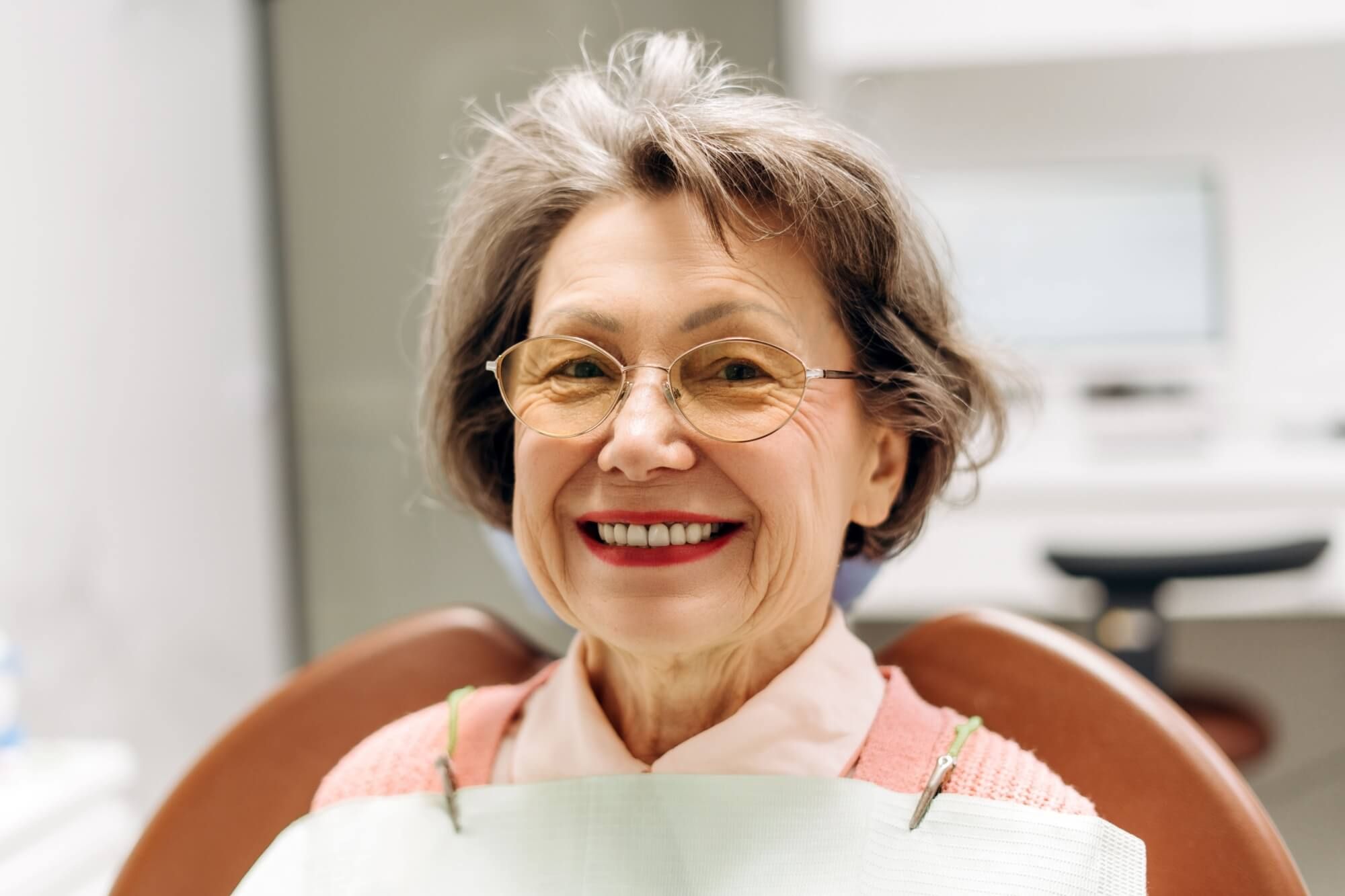 Elderly woman with glasses smiling while seated in a dental chair