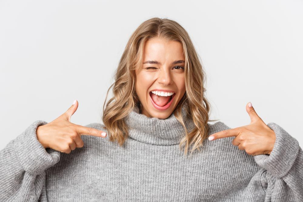 a person winking and smiling while wearing a chunky gray turtleneck