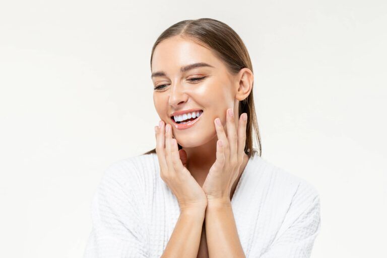 Smiling beautiful Caucasian woman touching her face on isolated studio white background for beauty and skin care concepts