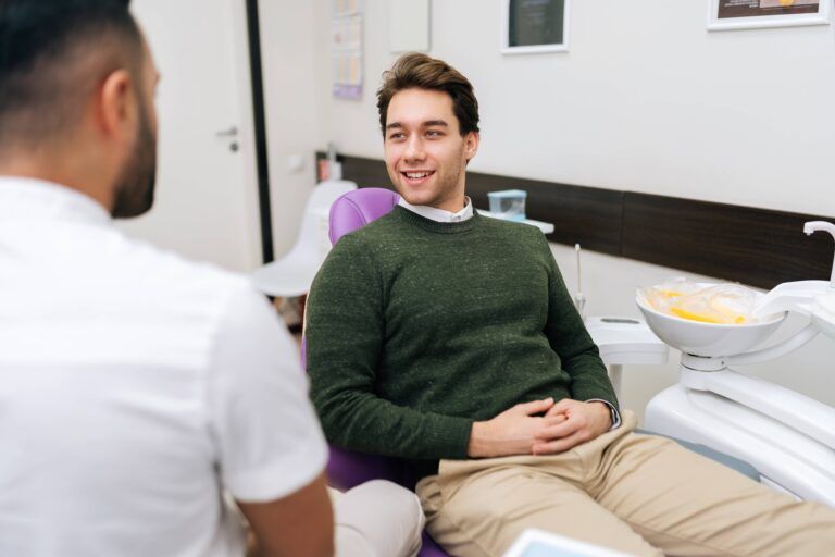 Portrait of cheerful bearded young man patient attentively listening unrecognizable male dentist discusses treatment plan