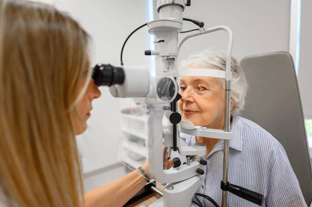 Female doctor using slit lamp to examine senior woman's eyes during vision test at modern ophthalmology clinic