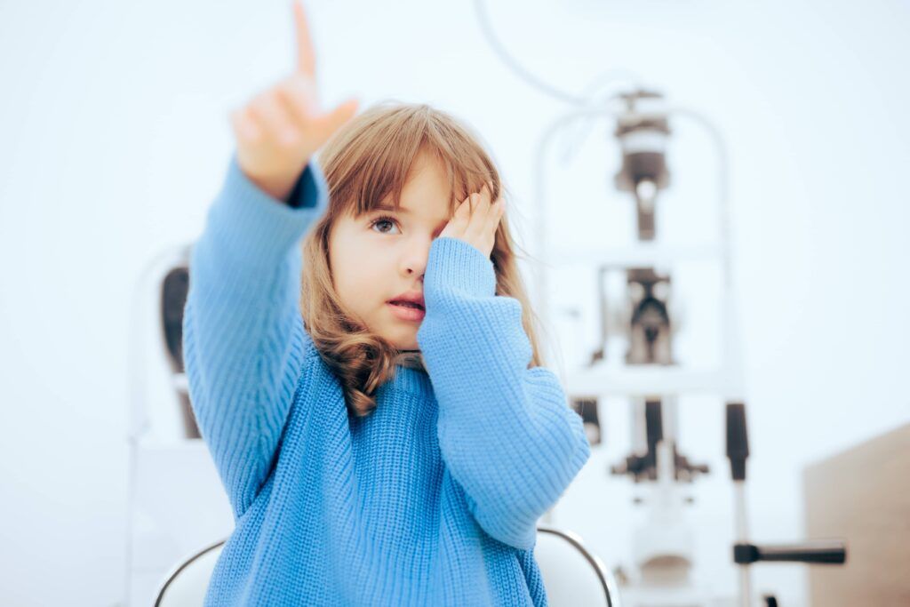 Cute Little Girl Covering One Eye During Ophthalmological Consult. Toddler child pointing to a vision chart during eye check