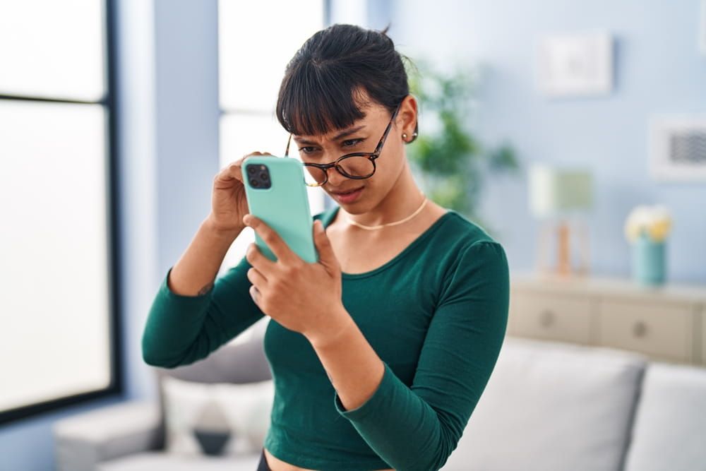 Young beautiful hispanic woman looking screen smartphone with vision problem at home