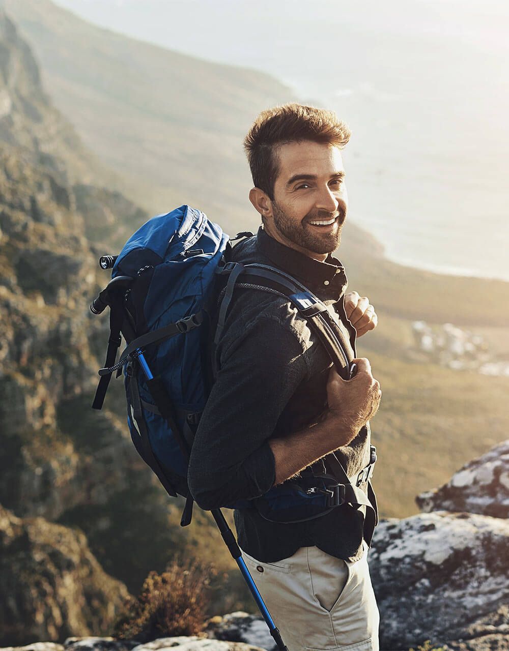 Portrait, mountains and hiking with man, smile and journey with nature, sunshine and getaway trip.