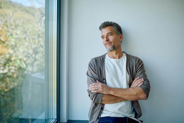 Thoughtful man with crossed arms looking through window, contemplating ideas, reflecting on life, finding inspiration