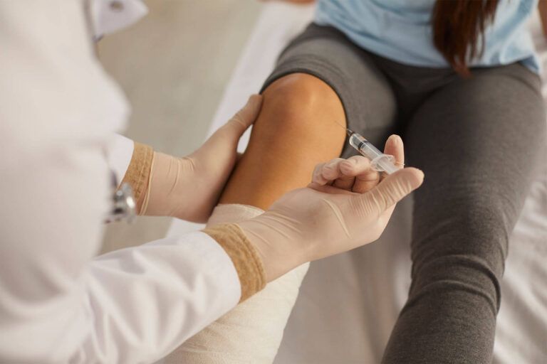 Close up of a doctor giving an injection in the knee to a patient who has an injured leg.