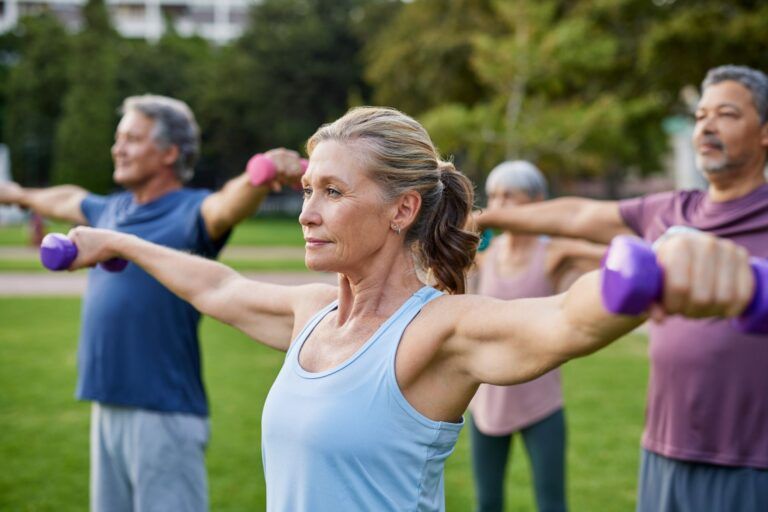 Elderly people lifting small weights at park. Focused senior woman working out with group of friends.