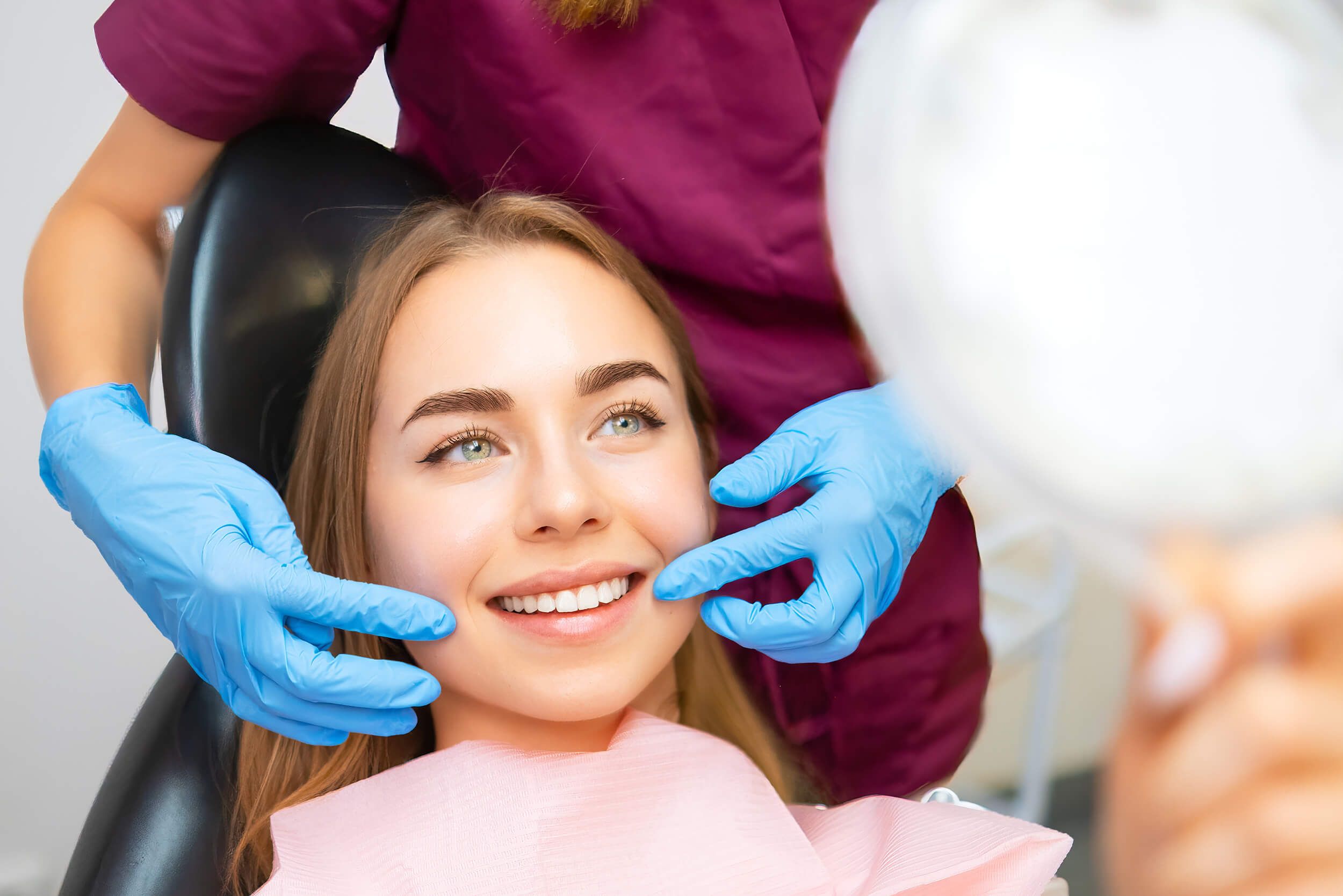 a patient examining her smile in a mirror while being attended to by a dental professional