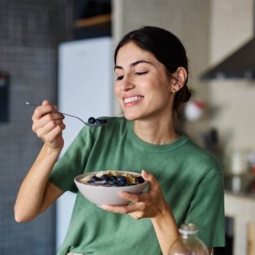 Portrait of a young woman preparing and eating breakfast, drinking juice in the kitchen at home