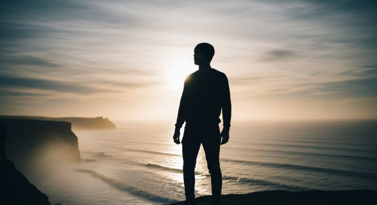 Silhouette of person standing on a coastal cliff or near ocean horizon, arms relaxed, looking out to sea,