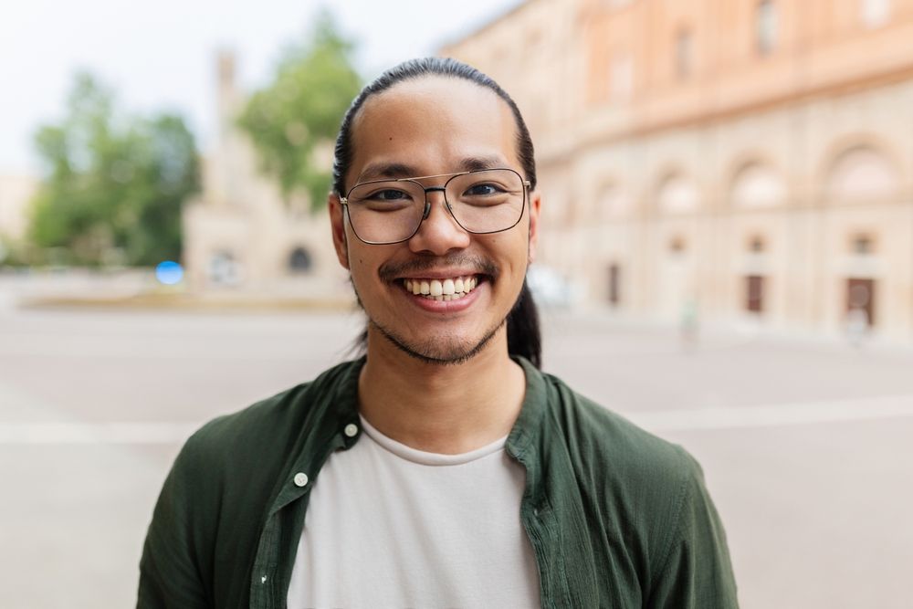Smiling portrait of young Asian man looking at camera standing at city street.