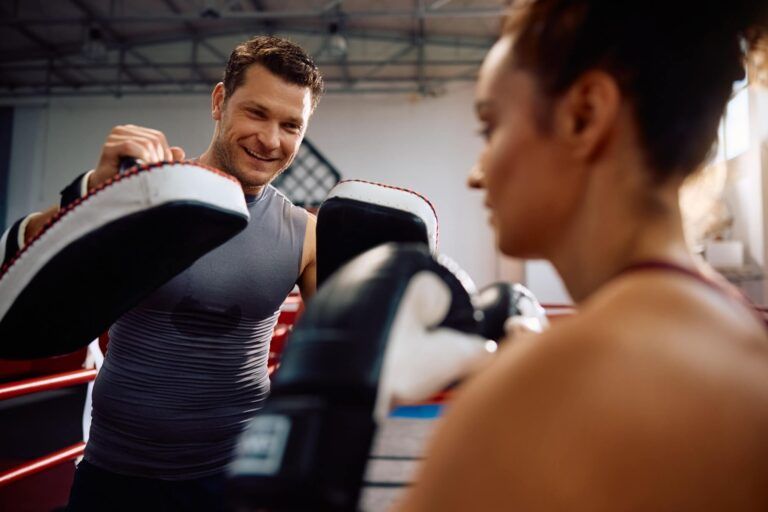 Happy boxing coach and female fighter having sports training in health club.